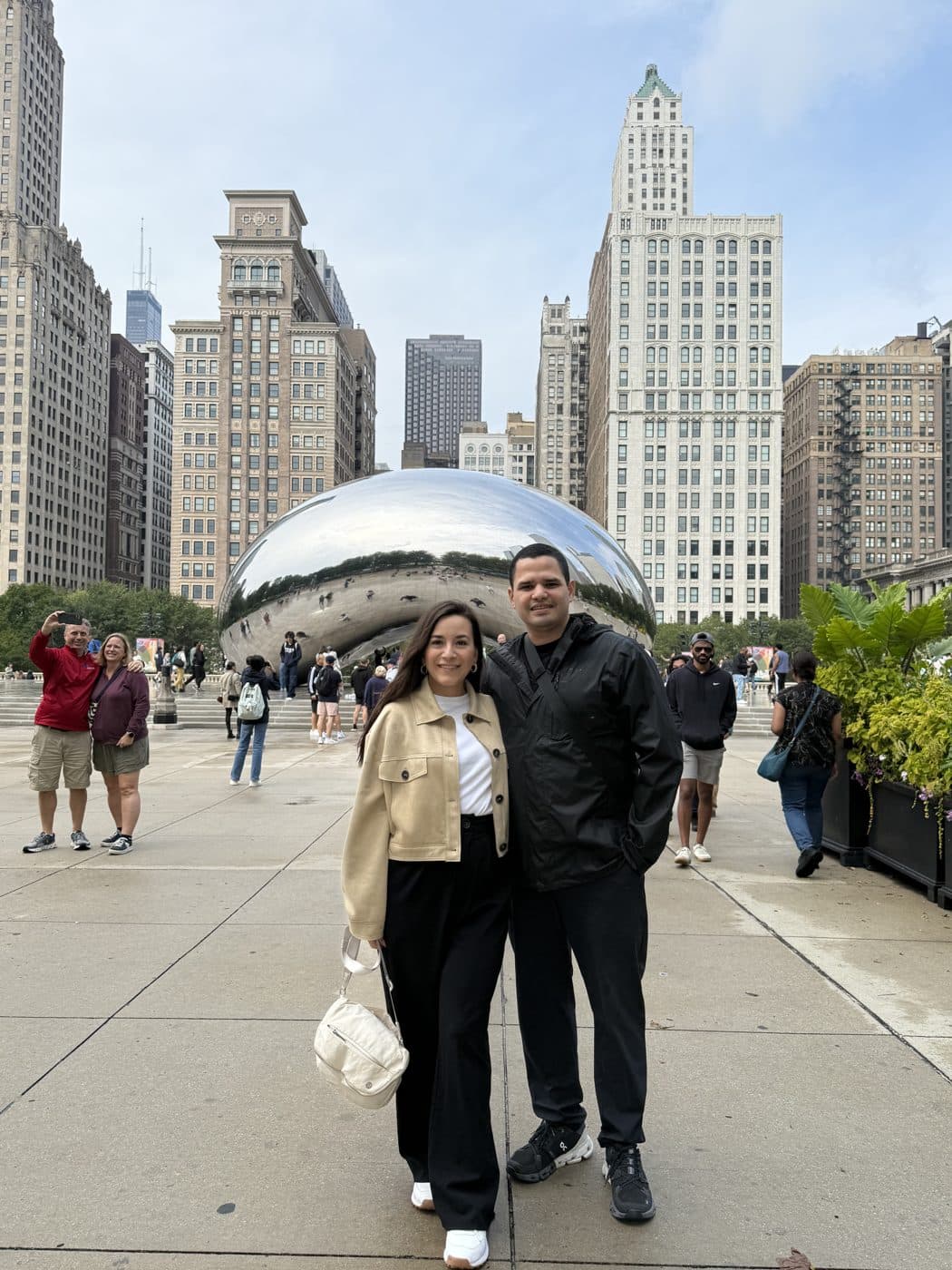 Adriana and Yair in a plaza, a mirrored sculpture and skyline behind them.