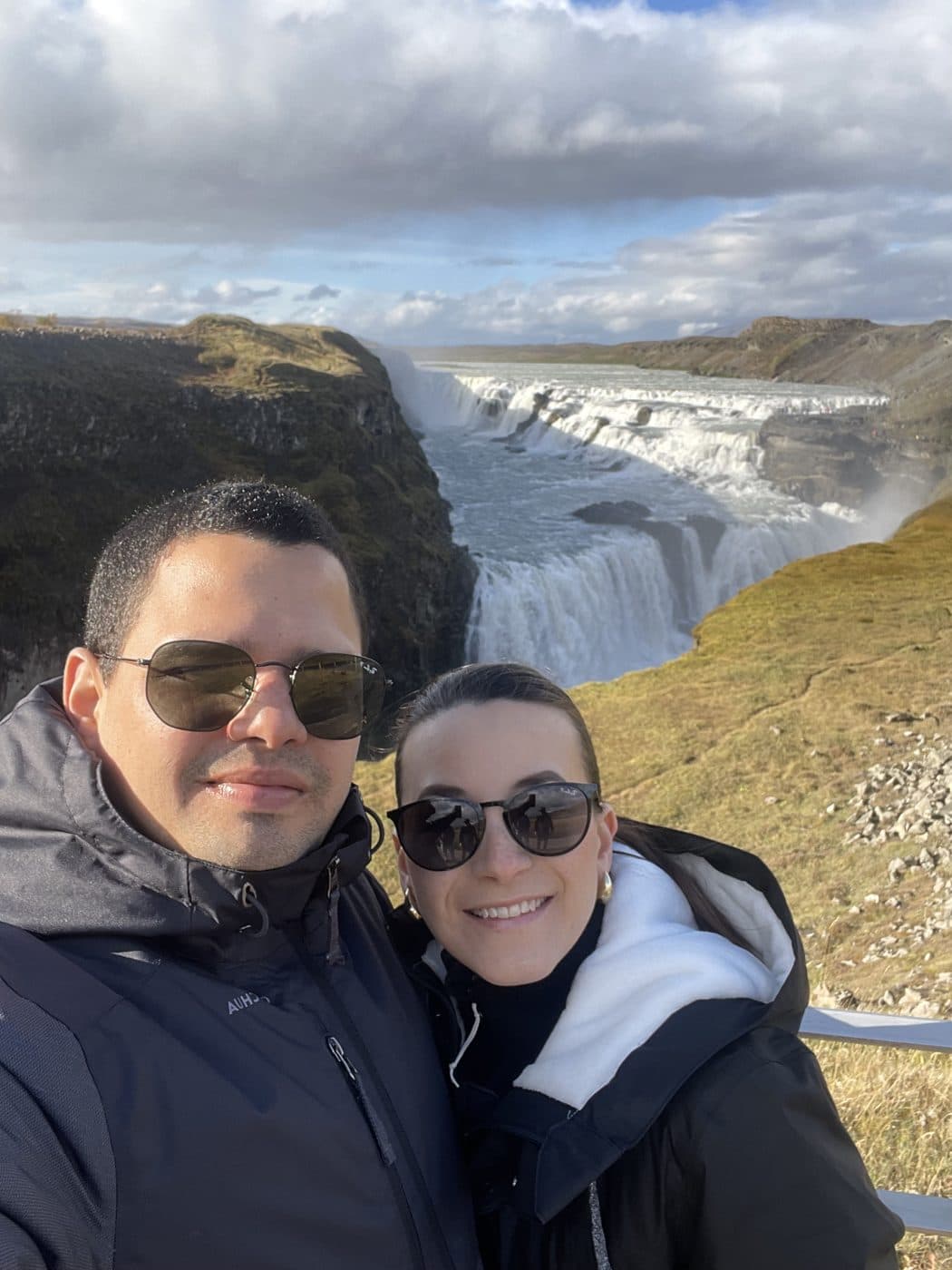 Adriana and Yair in coats, a waterfall and dark rock behind them.