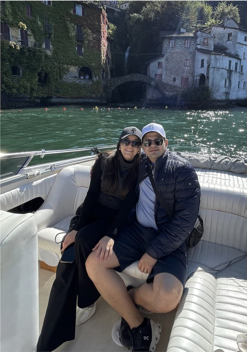 Adriana and Yair on a boat on Lake Como, a stone village on the shore behind them.
