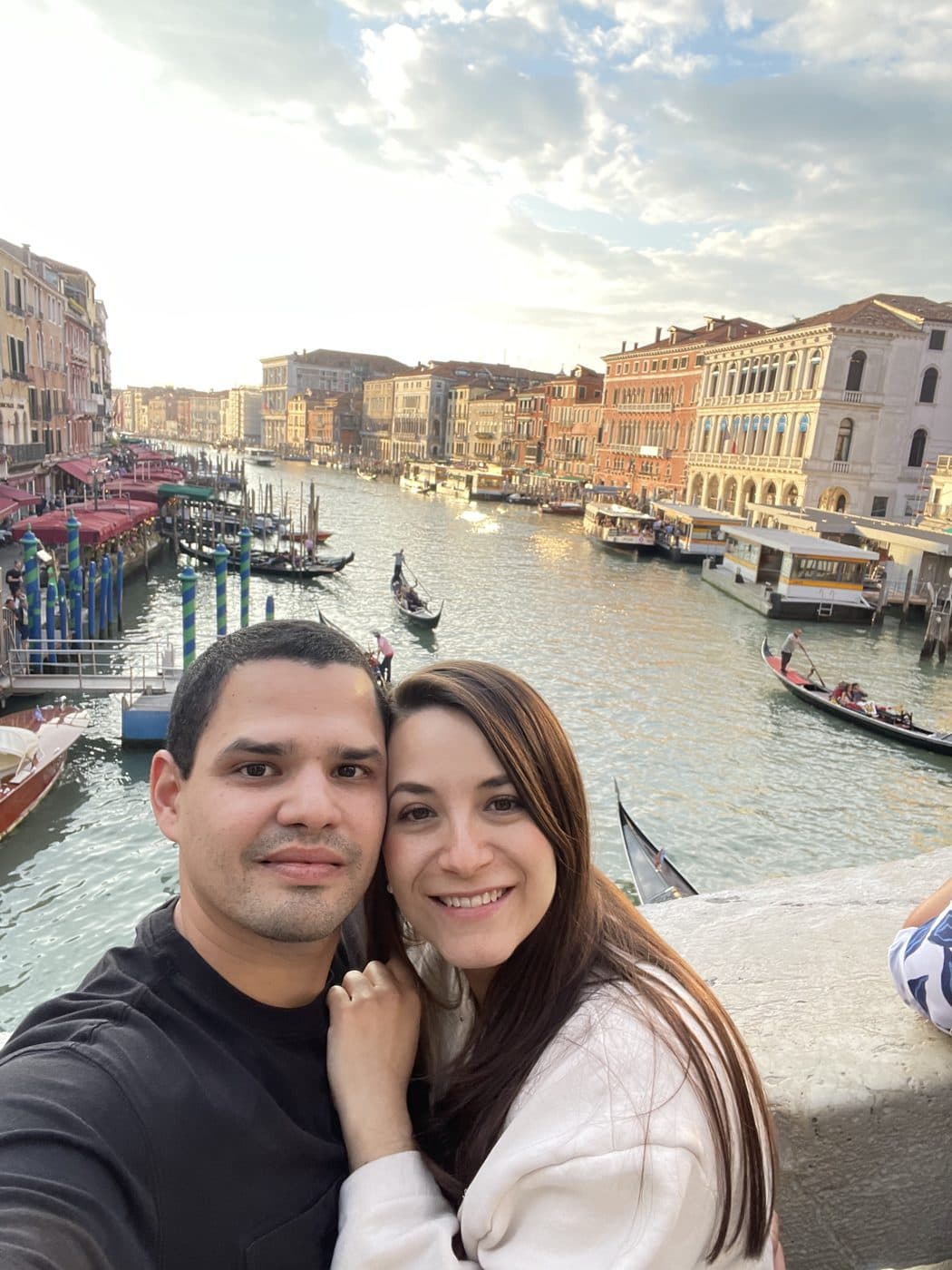 Adriana and Yair beside a canal lined with moored gondolas.